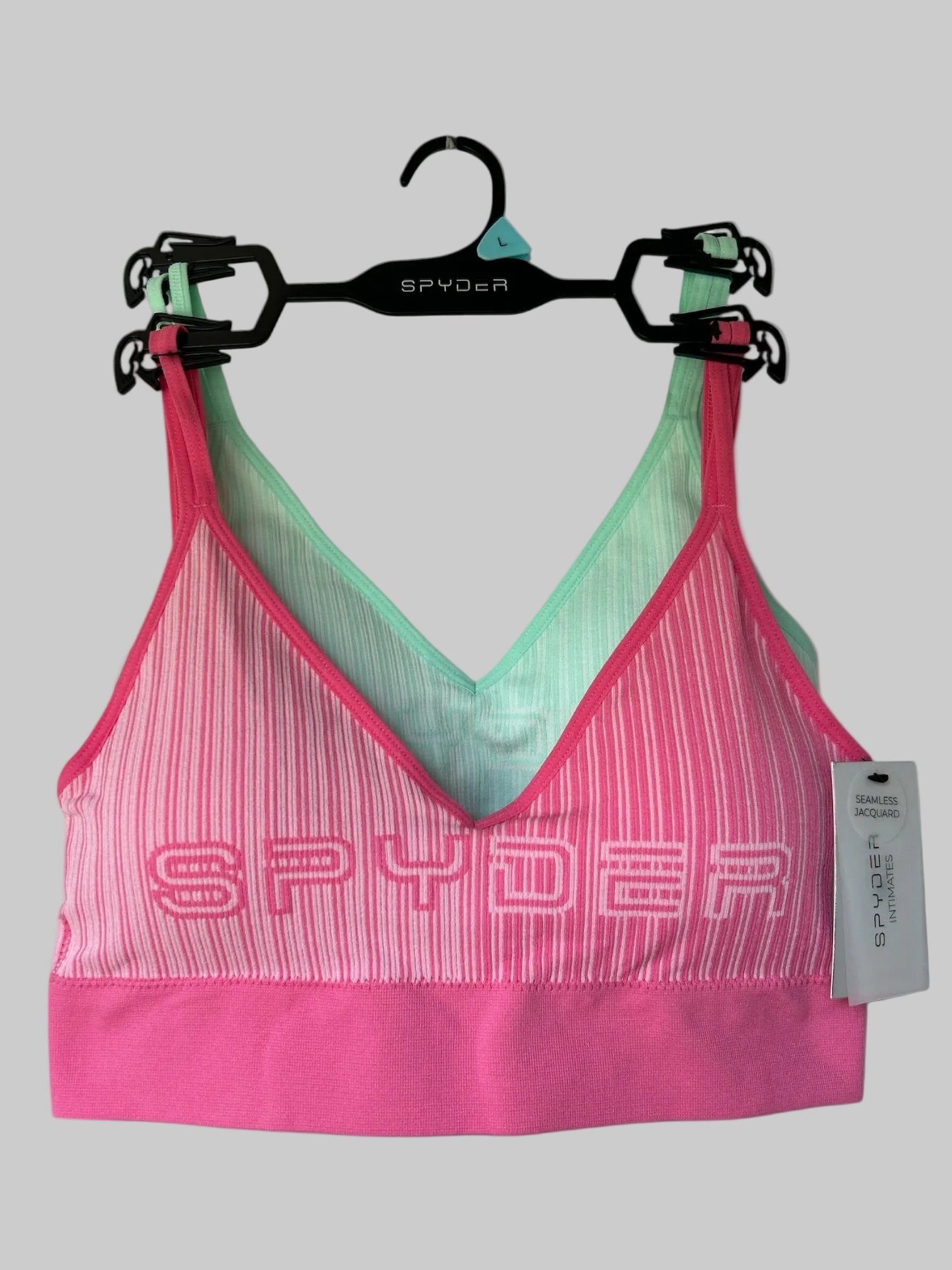 Pink and green sports bra with 'Spyder' branding on a hanger against a white background.