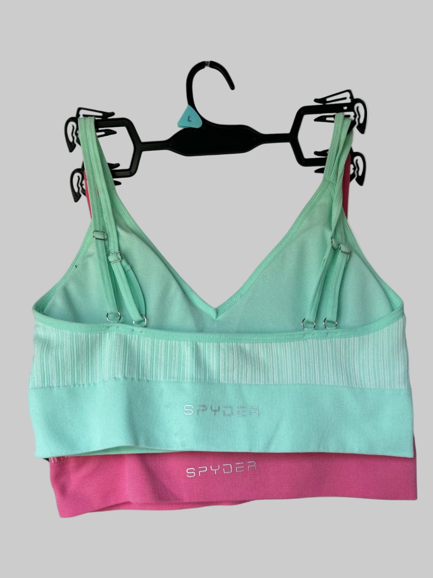 Green and pink sports bra with 'Spyder' branding on a hanger against a white background